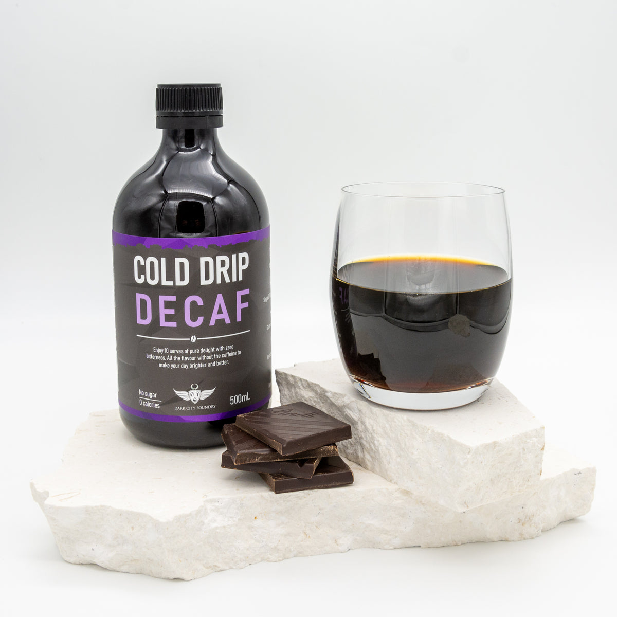 glass of decaf cold drip coffee pictured with a 500ml bottle of decaf cold drip coffee and a few pieces of chocolate