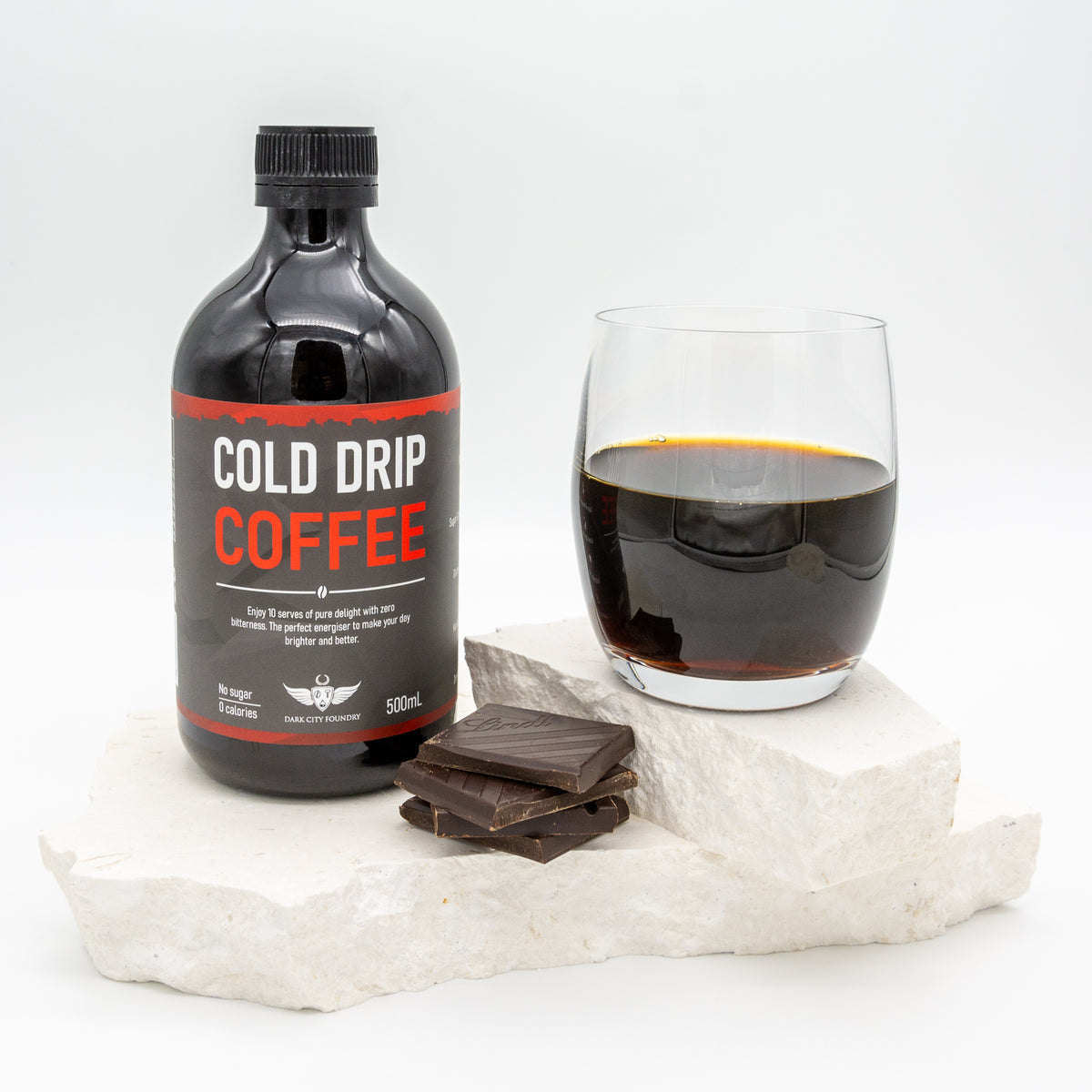 bottle of cold drip coffee pictured with a glass of coffee next to it and a few pieces of chocolate